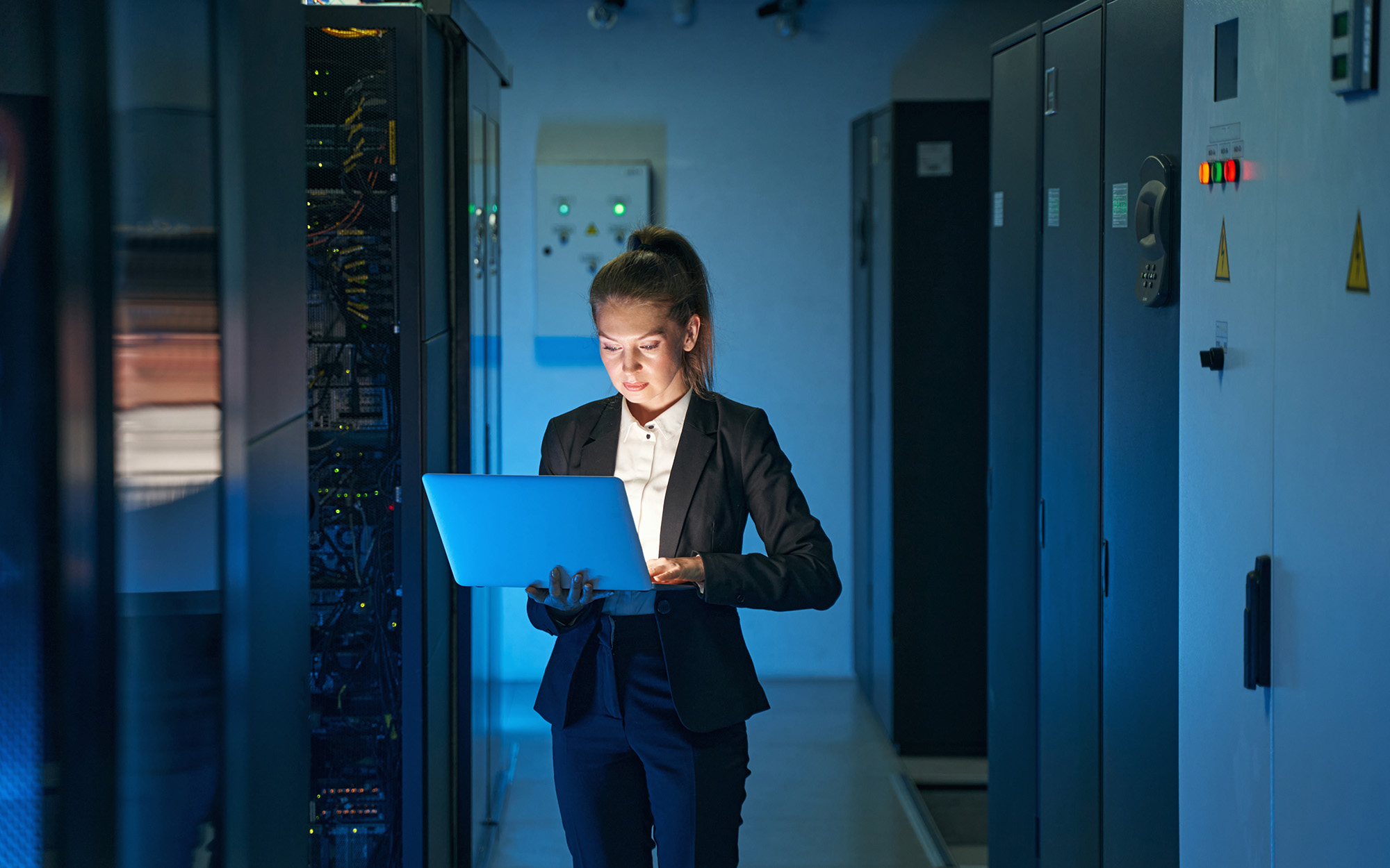 Woman in Server Room with Blue Lighting Using Laptop