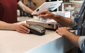 Cropped photo of caucasian man paying debit card in cafe while waiter holding payment terminal