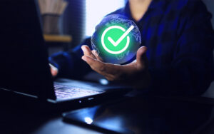 Hand holding globe and correct green checkmark while working on laptop computer screen