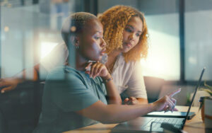 Side view of two professional women in modern office made of glass, looking at laptop and collaborating