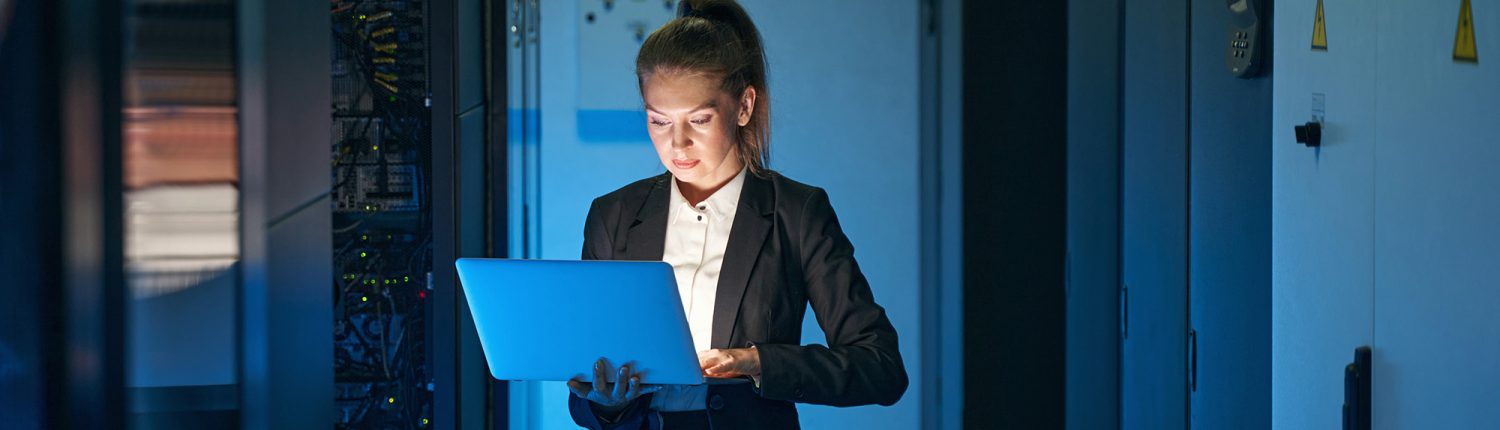 Woman in Server Room with Blue Lighting Using Laptop