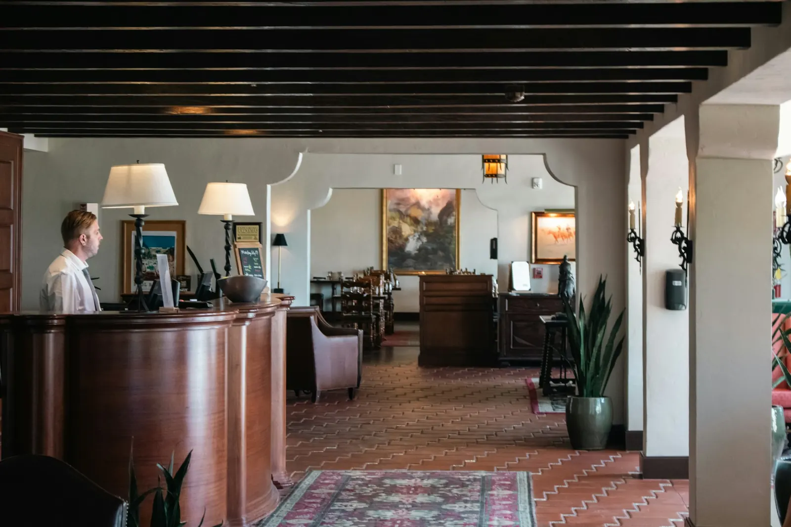Hotel clerk working at the front desk computer in a warm, wood-panelled lobby